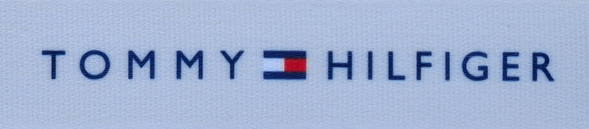 Logo von Tommy Hilfiger mit gesticktem Schriftzug auf hellem Hintergrund.
